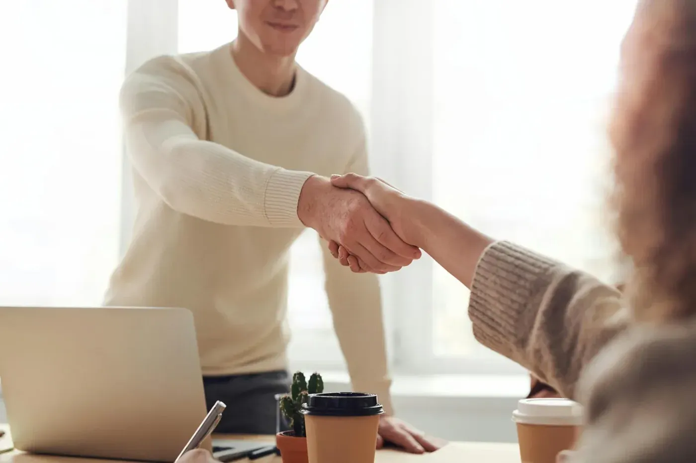 Zwei Personen geben sich über einem Schreibtisch die Hand
